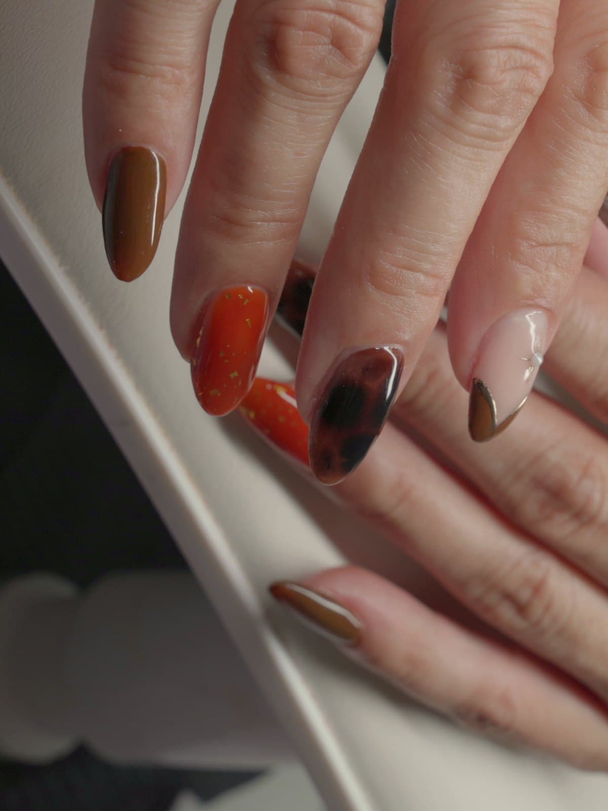 Set de uñas almendra terminado en naranja con destellos dorados, carey y francés nude en Statement Barbershop & Salon